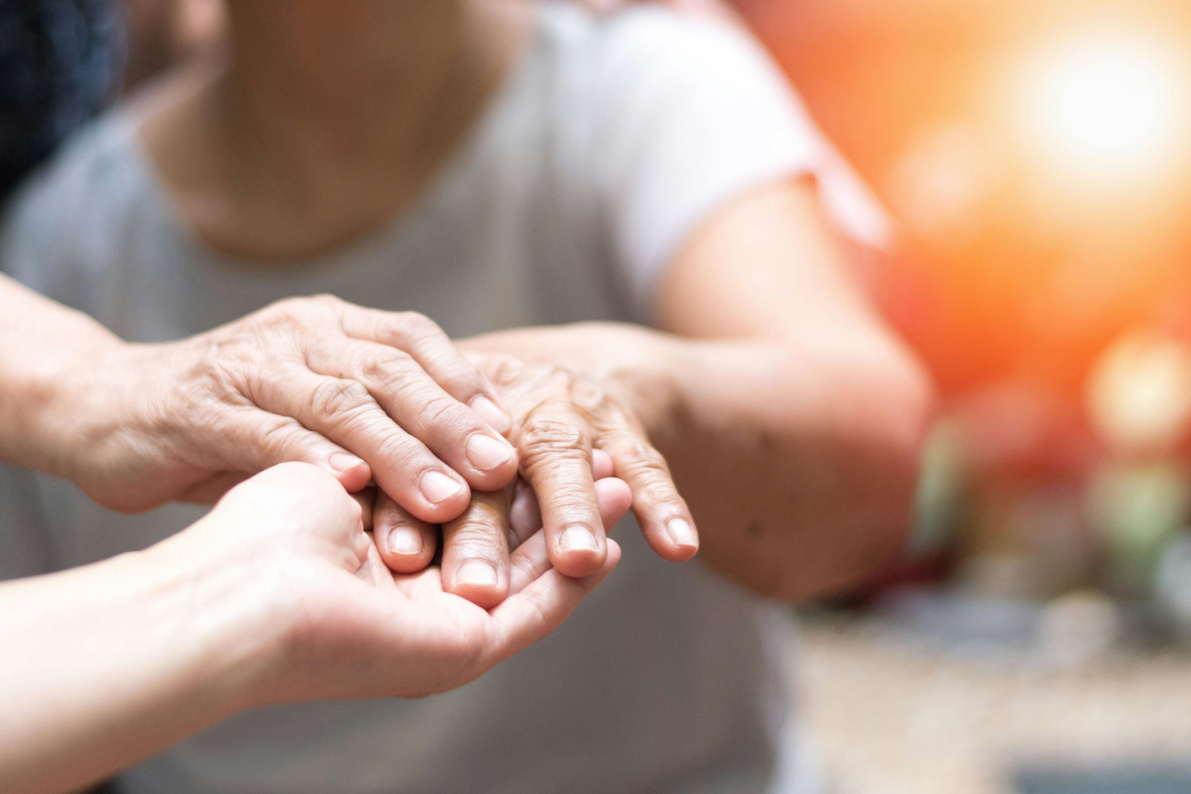 Caregiver holding hand of older adult with Parkinson's disease / Khunatorn - stock.adobe.com